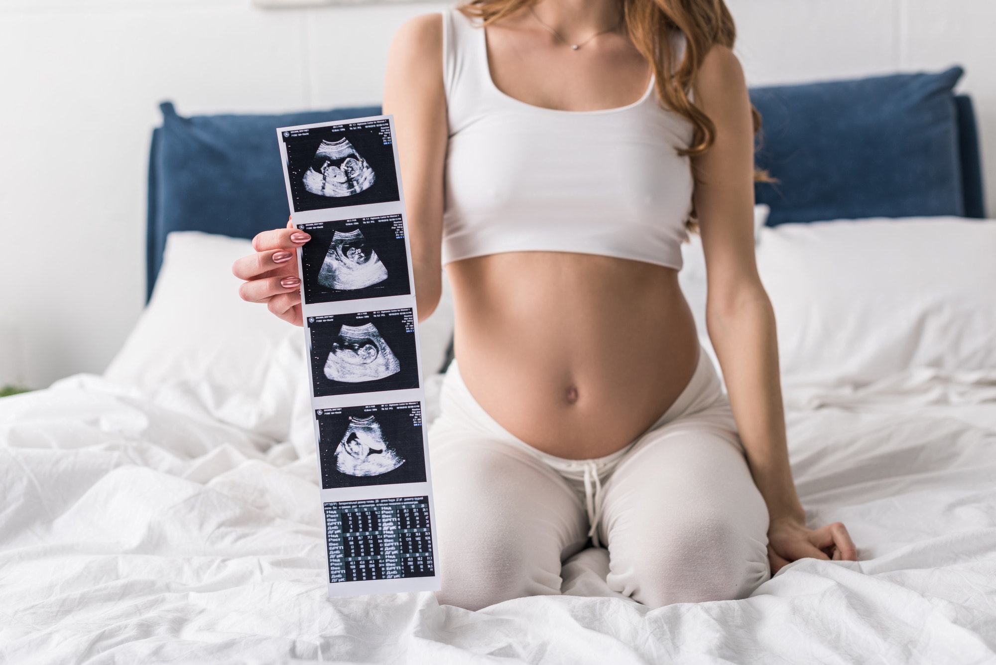 Cropped view of pregnant woman sitting on bed and showing ultrasound scans