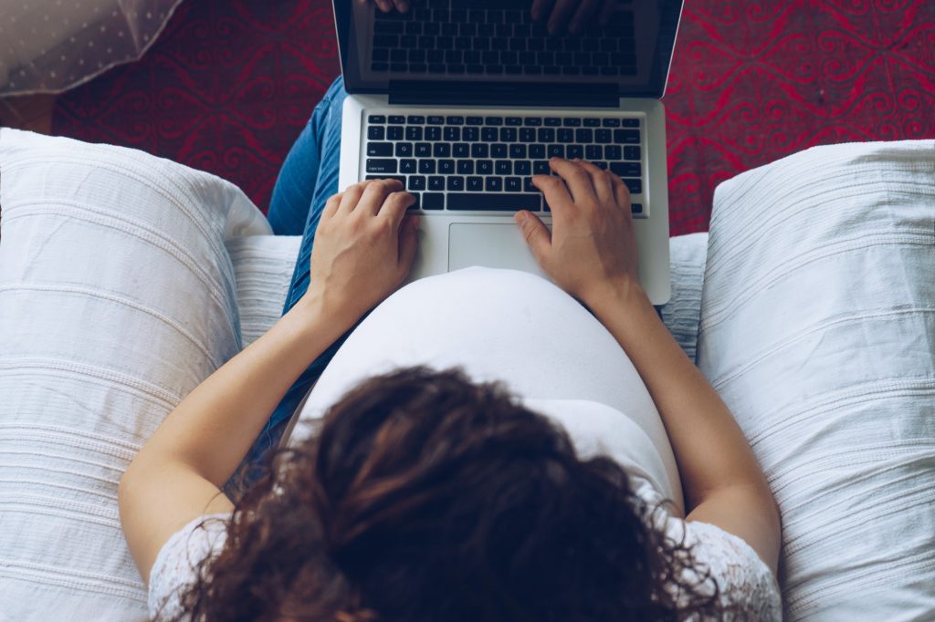 Pregnant woman holding laptop in her hands, top view